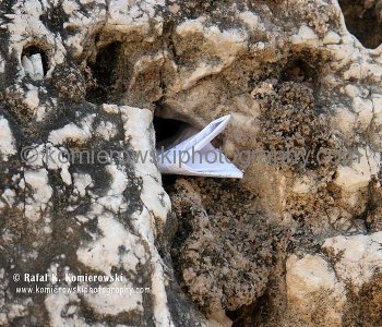The lower cracks of the chalky, yellow-white blocks have been stuffed with bits of paper containing written prayers.